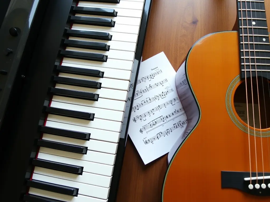 A piano keyboard beside a guitar and sheet music, symbolizing instrument comparison.