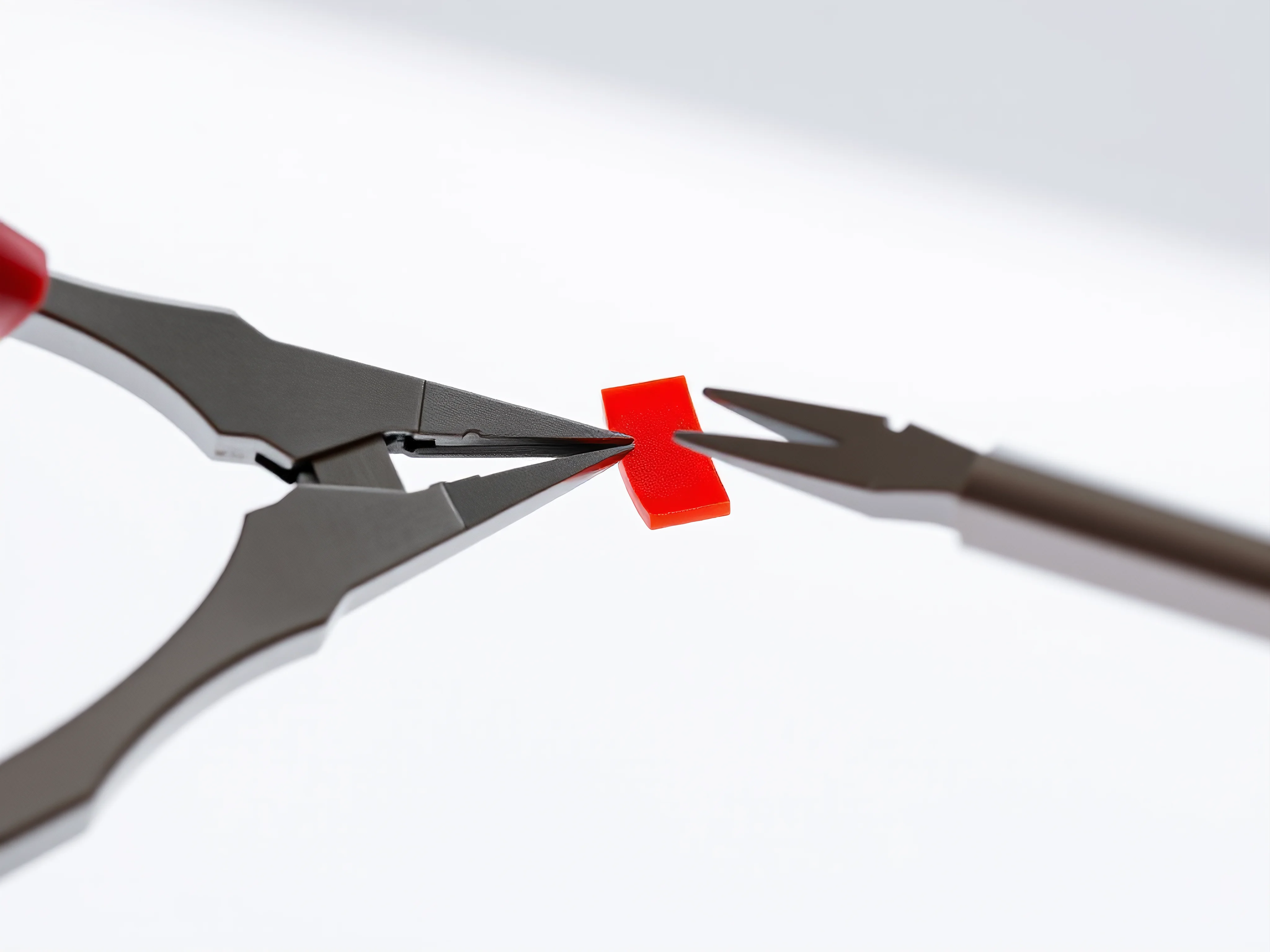Precision nippers cutting a vibrant red plastic model piece from a sprue on white.